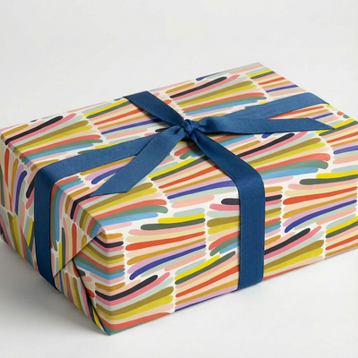 
                    
                      Rainbow Stripes wrapping paper, multi-color brush strokes on recycled paper, wrapped gift box with dark blue ribbon bow,…
                    
                  