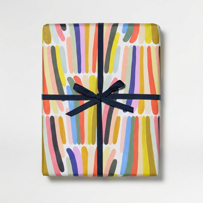 
                    
                      Rainbow Stripes recycled wrapping paper, abstract multicolored stripes, wrapped gift tied with dark blue ribbon, top-down…
                    
                  