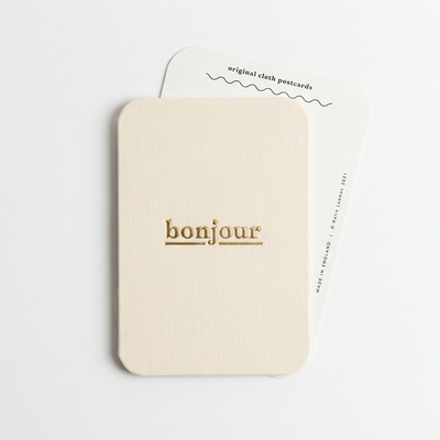 
                    
                      Katie Leamon "bonjour" Cloth-Covered Postcard, cream cotton cloth with gold foil lettering, front view with back of second…
                    
                  