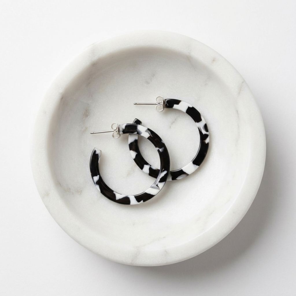 Sol hoop earrings, black & white tortoise acetate with silver posts, flat lay pair in a white marble dish.