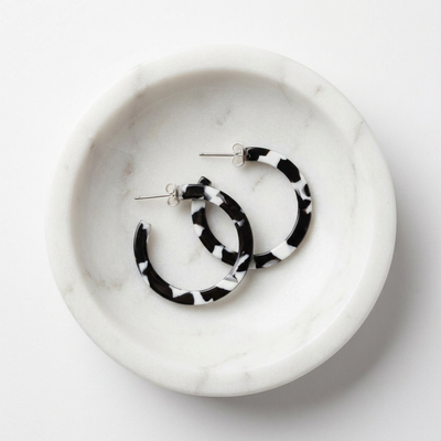 
                    
                      Sol hoop earrings, black & white tortoise acetate with silver posts, flat lay pair in a white marble dish.
                    
                  