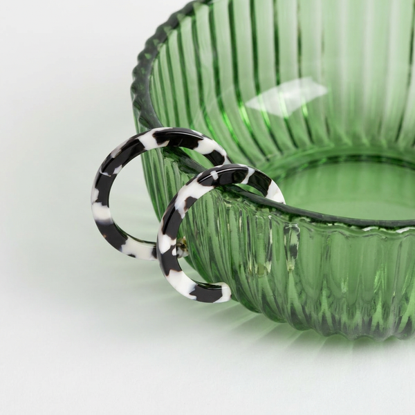 NAT + NOOR Sol hoop earrings, black and white tortoise cellulose acetate, pair hanging on a green ribbed glass bowl.