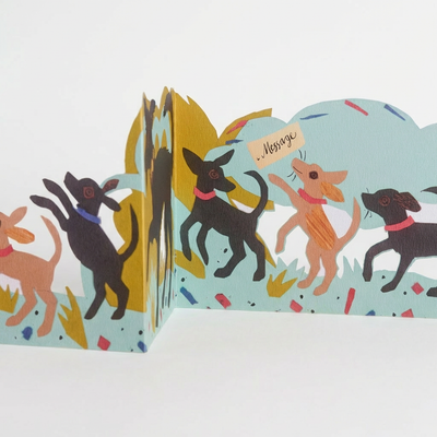 
                    
                      Puppy Parade die-cut card, multi-layered view of illustrated black and tan dogs with 'Message' tag, standing folded depth.
                    
                  