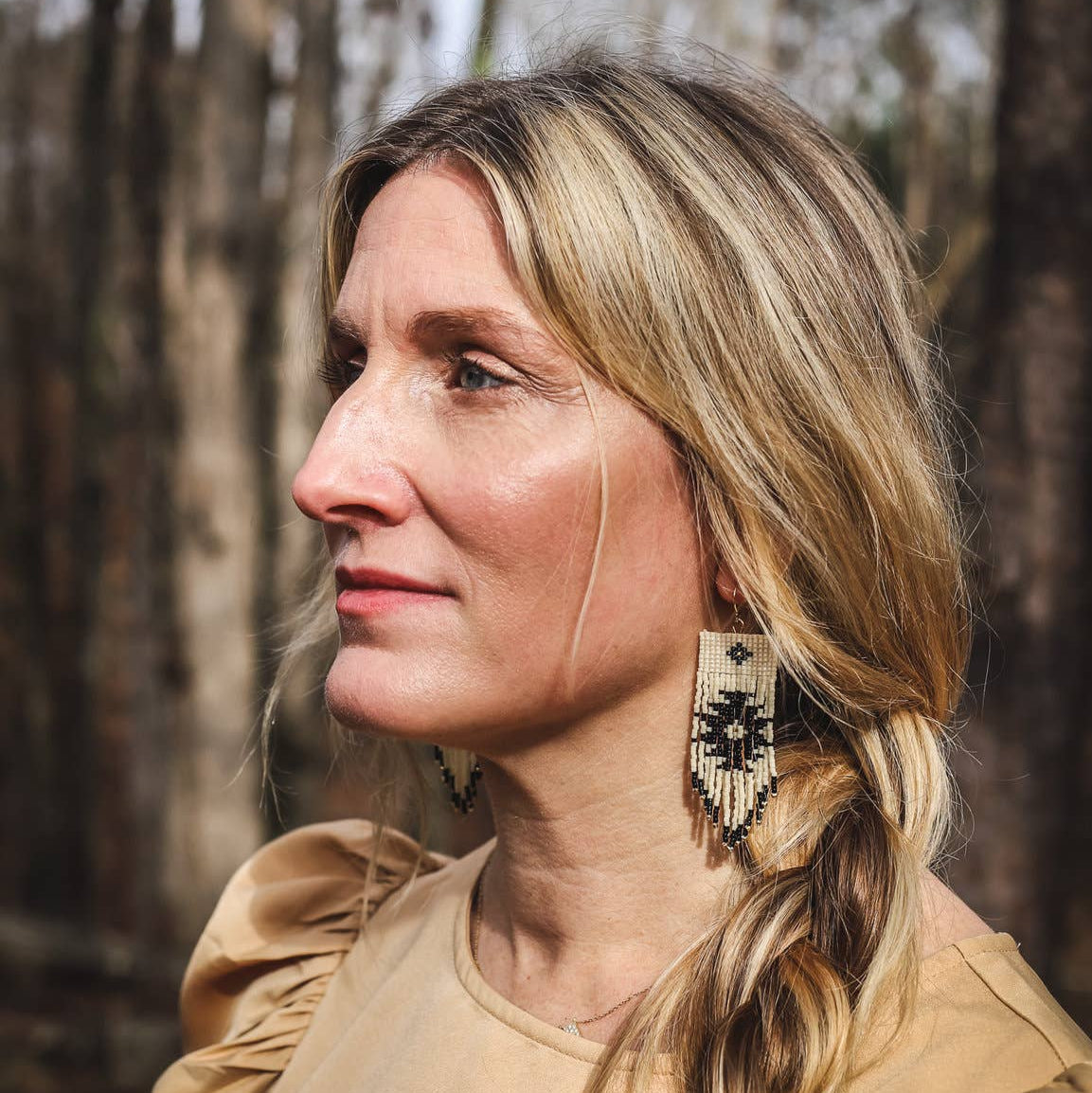 Woman with braided hair and earrings standing in a forest