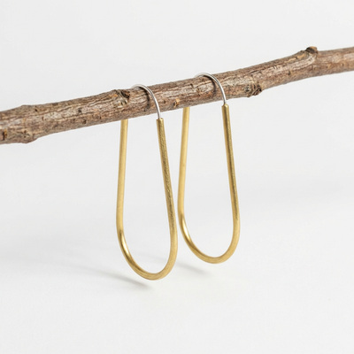 
                    
                      Modern Madini Long Hollow Brass Hoops, U-shaped raw brass earrings with silver-toned posts, hanging from a natural twig.
                    
                  