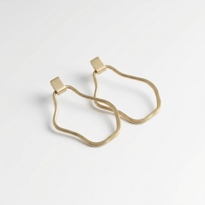 
                    
                      Modern Madini Organic Circle Dangle Hoop Studs, raw brass, flat lay pair on white.
                    
                  