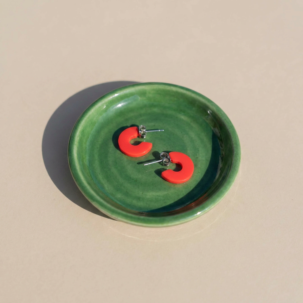 Mali Cherry Red hoop earrings, cherry red cellulose acetate, with visible stainless steel posts, pair resting in a green…
