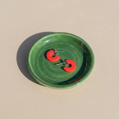 
                    
                      Mali Cherry Red hoop earrings, cherry red cellulose acetate, with visible stainless steel posts, pair resting in a green…
                    
                  