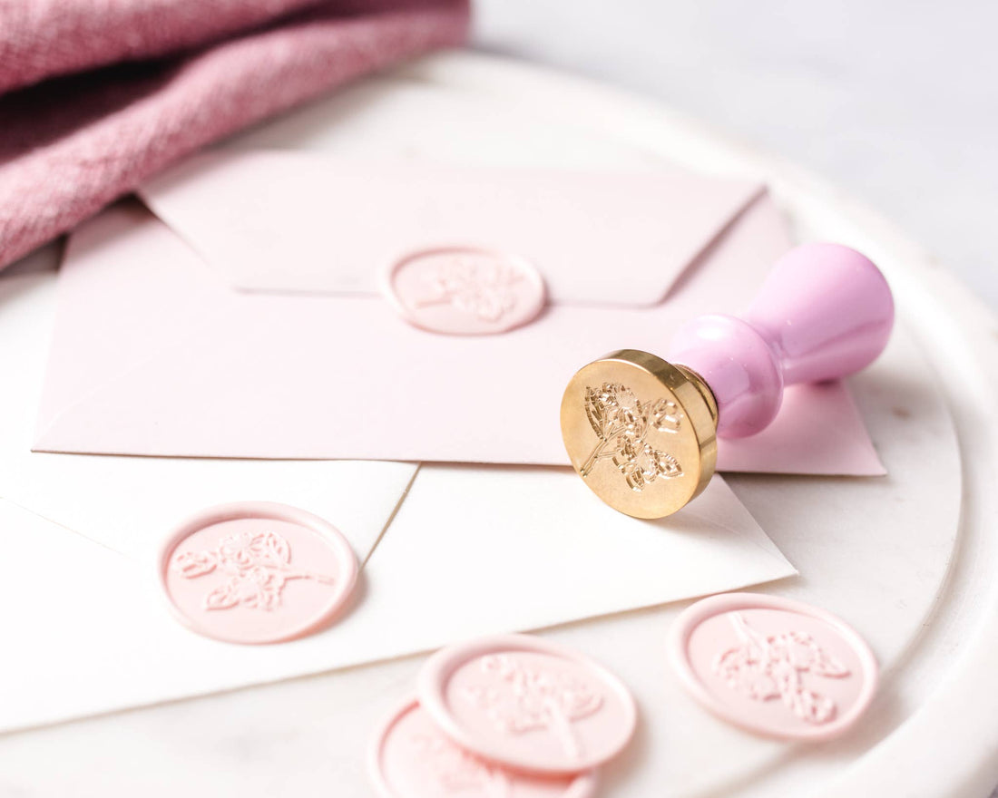 Wax Seal Stamp Set, gold brass stamp with pink handle, next to several floral pink wax seals on light pink and white…