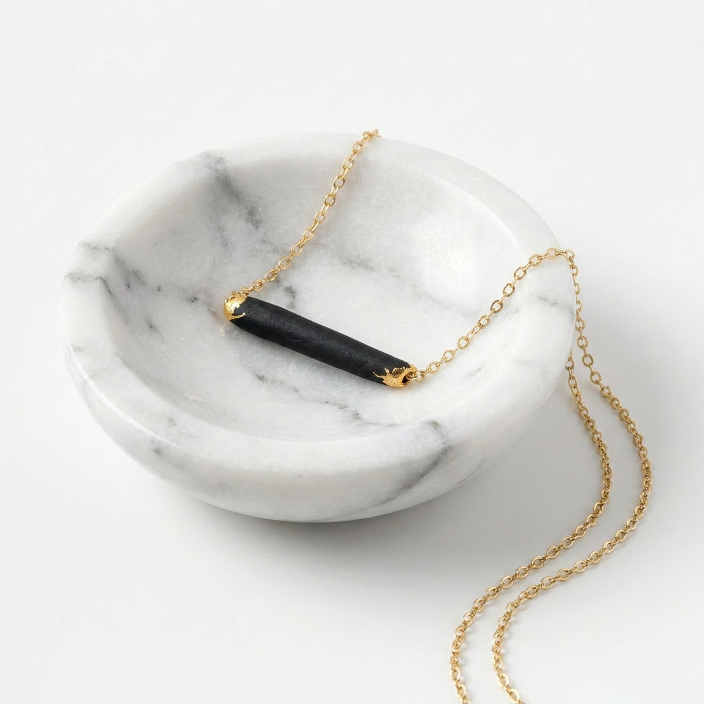 Gold necklace with a black porcelain fired pendant on a marble surface