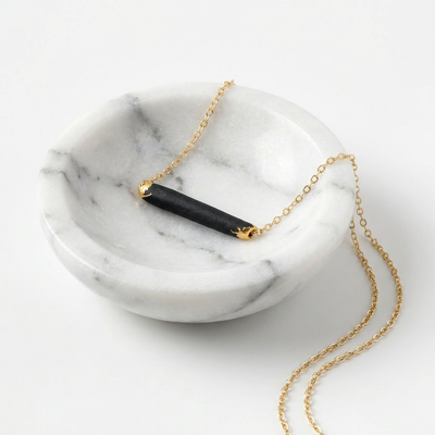 
                    
                      Gold necklace with a black porcelain fired pendant on a marble surface
                    
                  