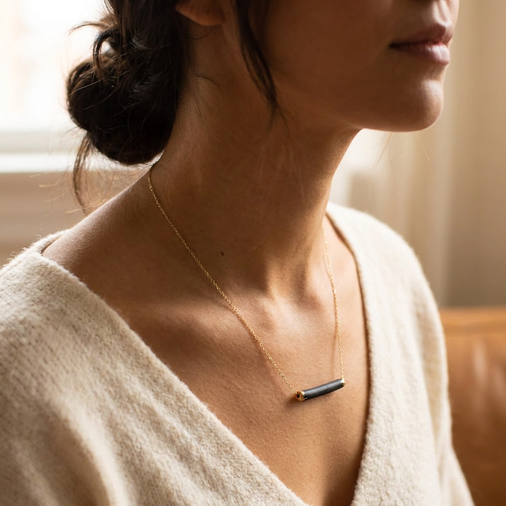 Woman wearing a gold necklace with a black porcelain pendant in a softly lit room.