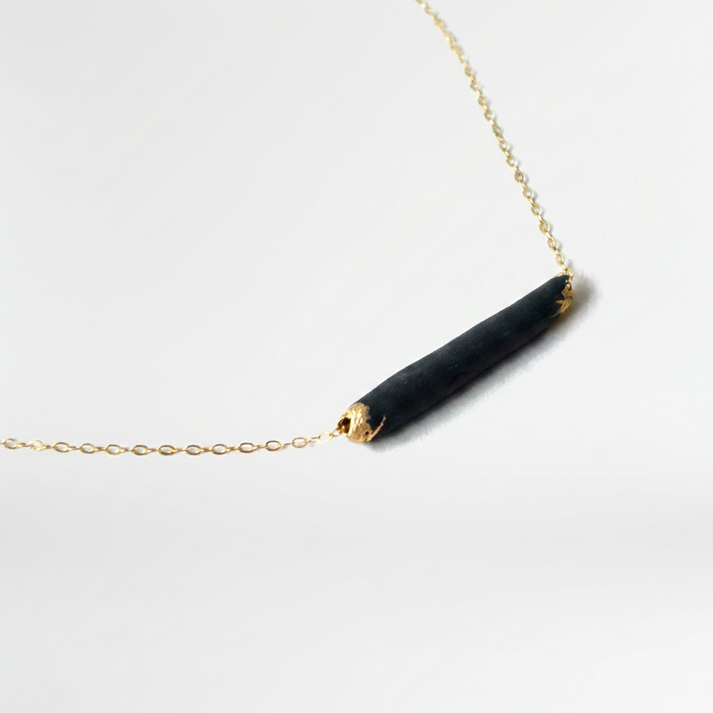 Bar necklace, matte black porcelain pendant with gold-dipped ends, 14k gold-filled chain, angled close-up.