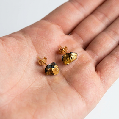 
                    
                      Gold Ore Studs, hand-formed porcelain stud earrings with 22k gold luster and black accents, held in hand for scale.
                    
                  