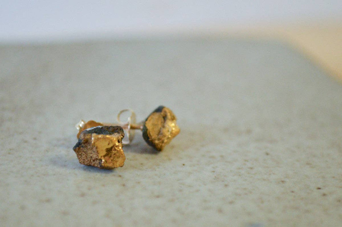 Gold stud earrings on a textured surface with a neutral background