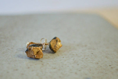 
                    
                      Gold stud earrings on a textured surface with a neutral background
                    
                  