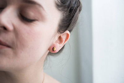 
                    
                      Close-up of a person wearing gold earrings with a neutral background
                    
                  