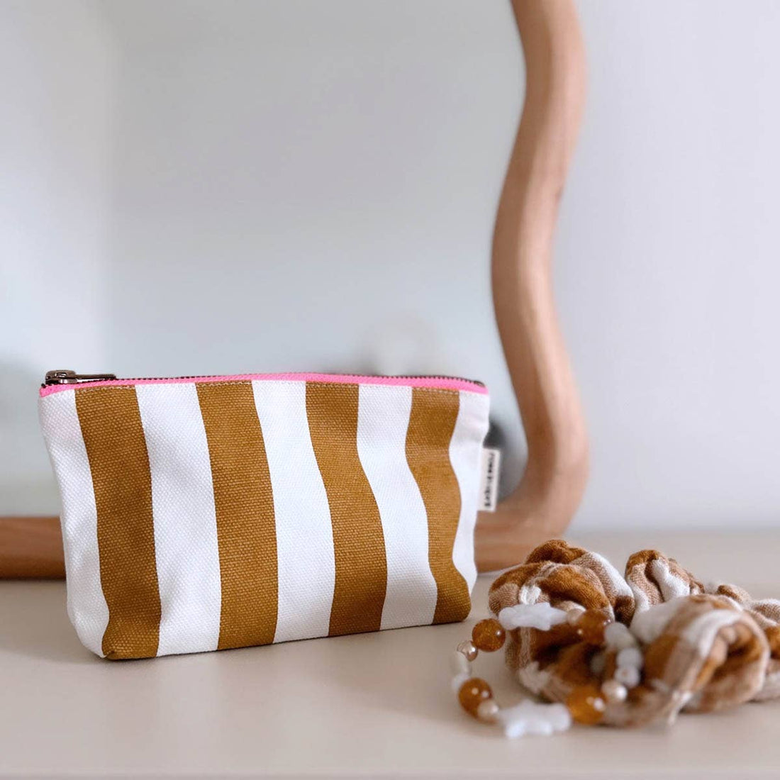 Sofia Pouch toiletry bag, caramel and white striped cotton canvas with bright pink zipper, angled view on a light surface.