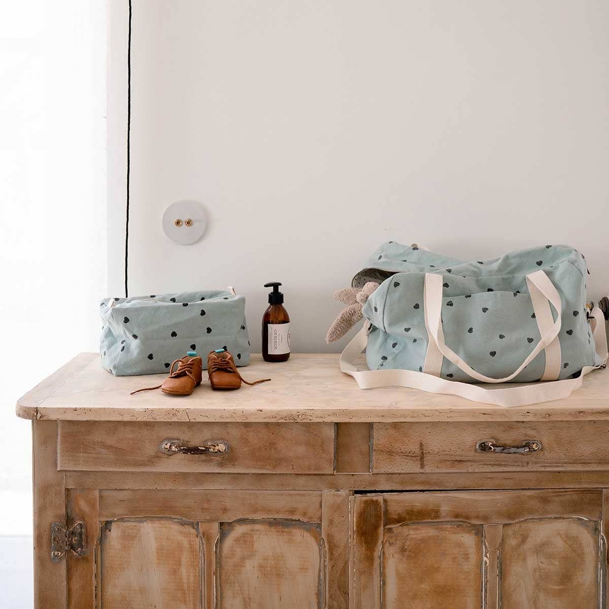 Rose in April: Vic Toiletry Bag (Blue Heart). Light blue polka-dotted bag and basket on a wooden dresser, with a bottle and shoes.