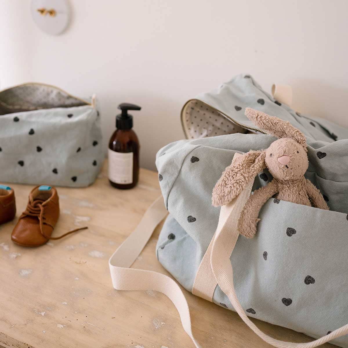 Rose in April: Vic Toiletry Bag (Blue Heart). Baby bag with plush toy, shoes, and a bottle on a wooden surface