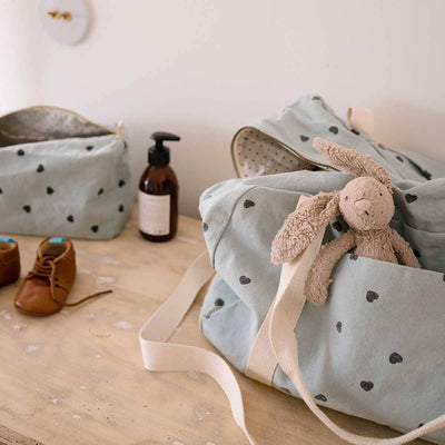 
                    
                      Rose in April: Vic Toiletry Bag (Blue Heart). Baby bag with plush toy, shoes, and a bottle on a wooden surface
                    
                  