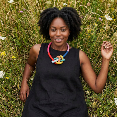 
                    
                      Water Bowline necklace, rainbow cotton yarn-wrapped cording, worn on model lying in a field of tall grass.
                    
                  