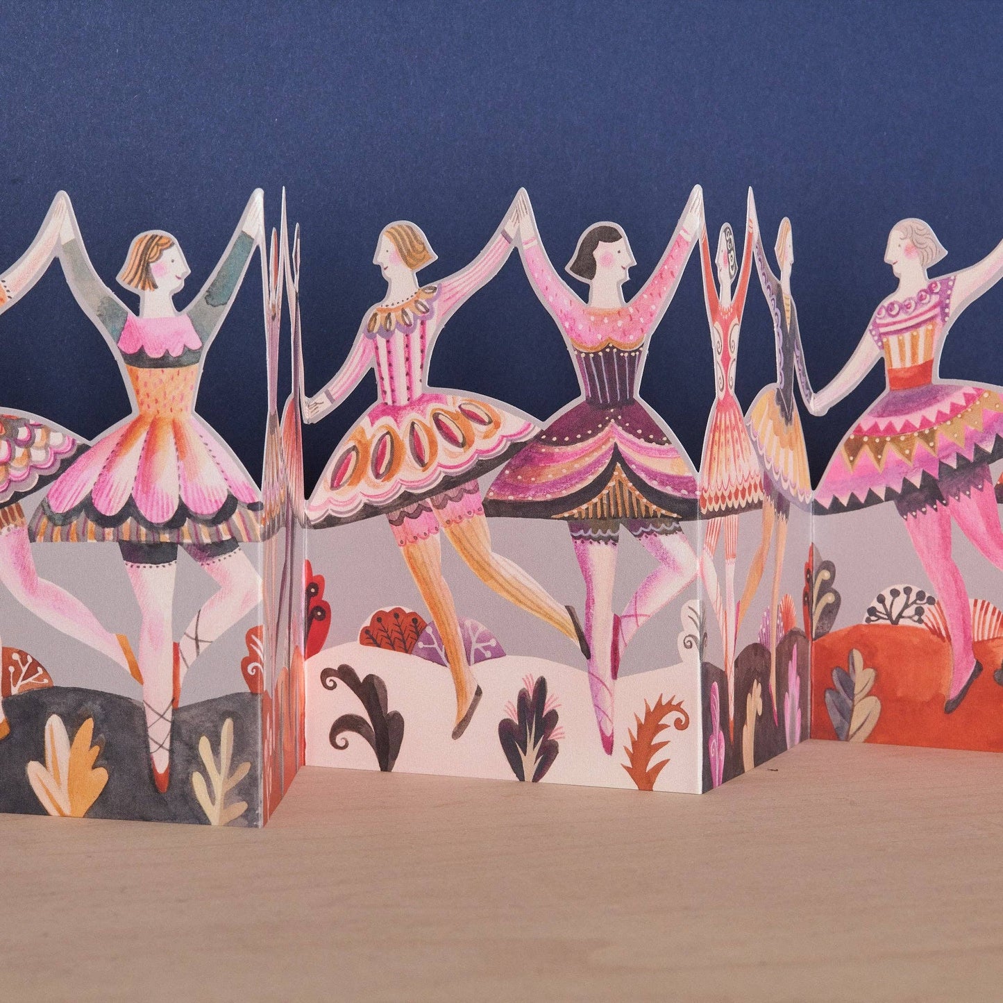Sarah Young Dancers Die-Cut Concertina Card. Colorful paper card of folk-art dancers set with a blue background