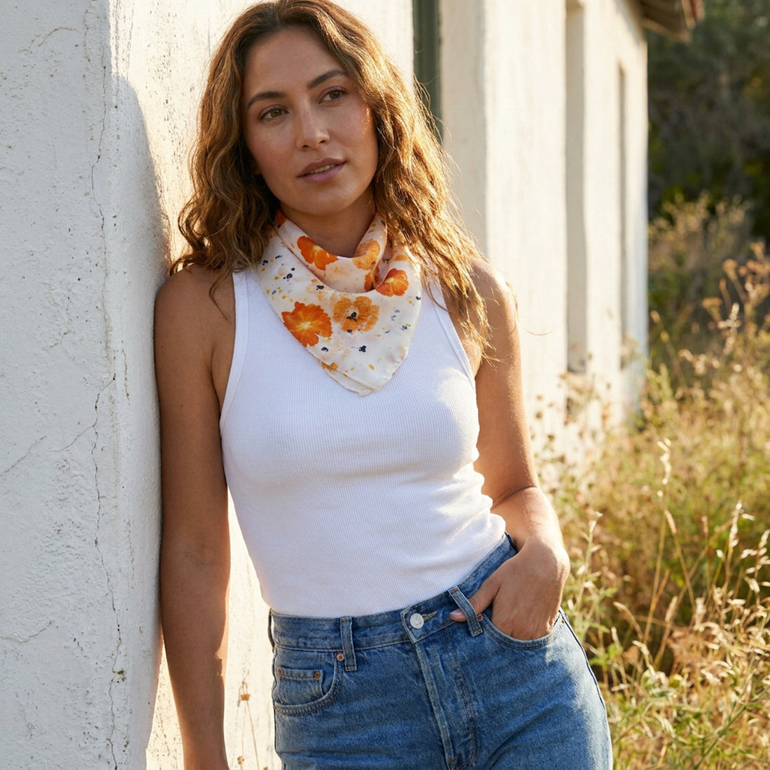 Abby silk bandana scarf, white with orange floral bundle-dye pattern, on model's neck in natural light.
