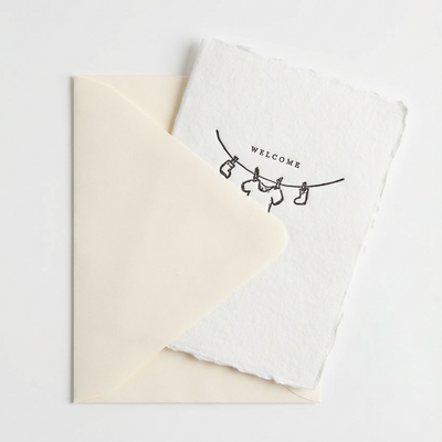 
                    
                      Welcome Baby greeting card, handmade white paper with deckled edge and clothesline design, peeking from cream envelope.
                    
                  