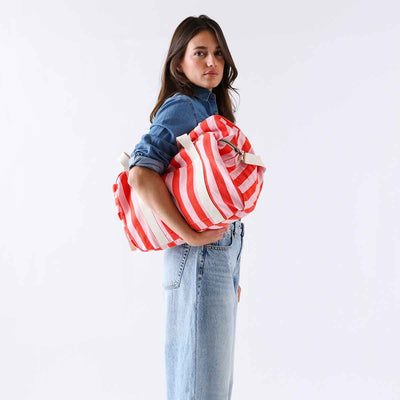 
                    
                      Raphael Weekend / Diaper Bag, tomato and candy pink striped cotton, held in model's arms, side view.
                    
                  