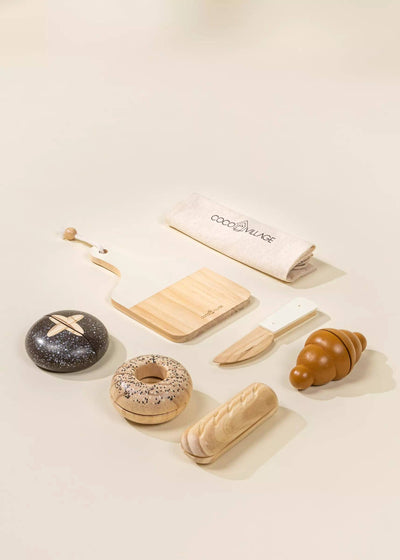 
                    
                      Coco Village Wooden Bakery Set toys, flat lay showing dark speckled bread, light wood donut, croissant, cutting board, knife.
                    
                  