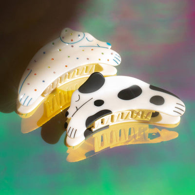 
                    
                      Two Puppy Claw dog hair clips, one white with black spots, one cream with colorful dots, matte cellulose acetate, flat lay…
                    
                  