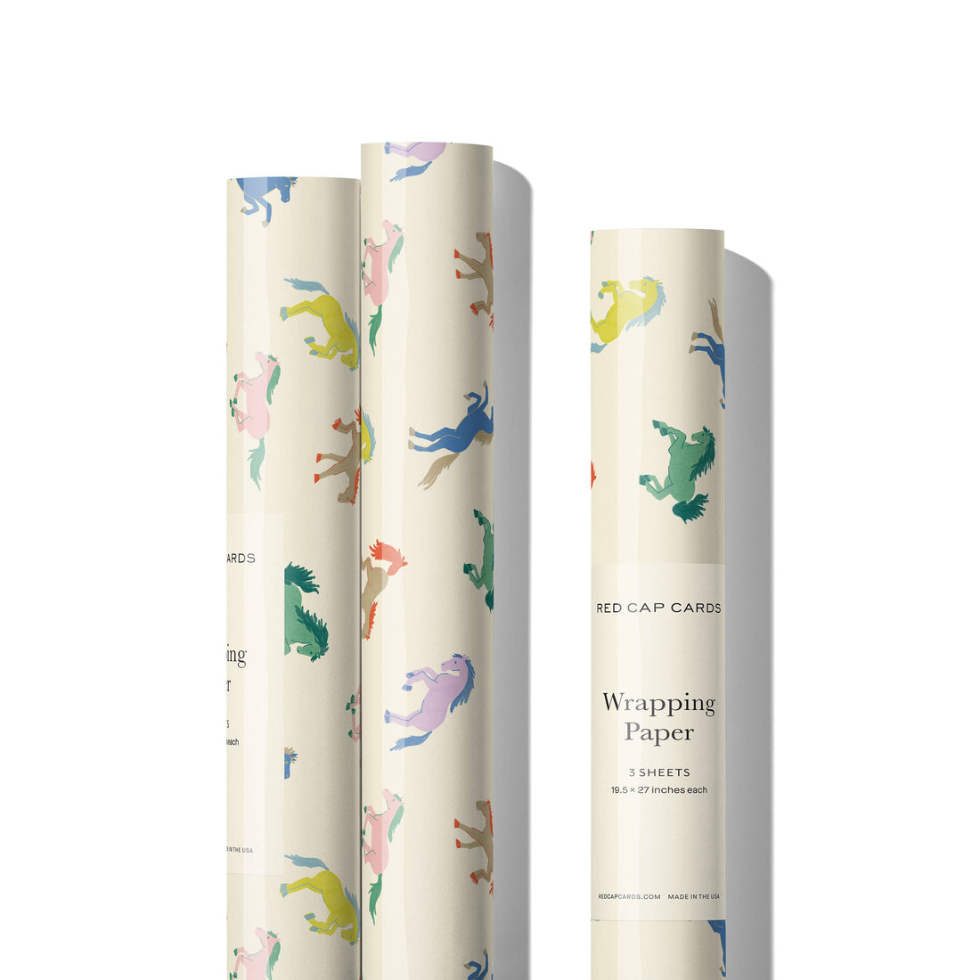 Wild Horses wrapping paper, three rolls standing upright with multicolored horses on cream recycled paper, showing label…