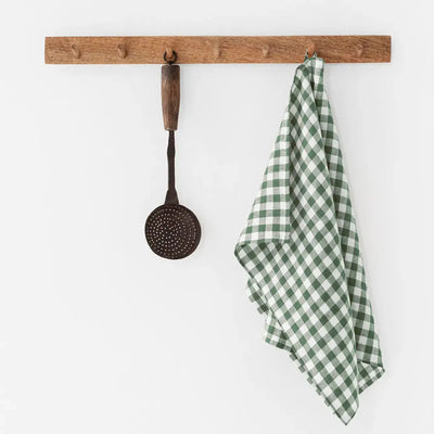 
                    
                      Green and white gingham 100% linen tea towel, folded and hanging on a rustic wooden peg rail, front view.
                    
                  