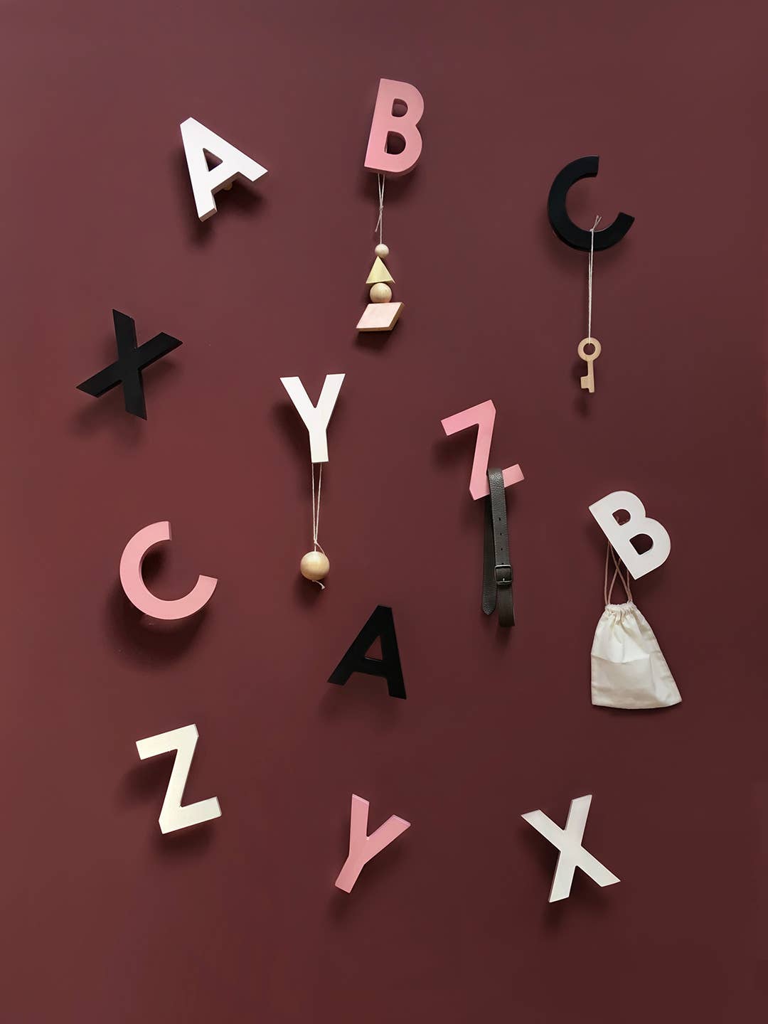 Alphabet Wall Hooks, black, white, pink solid beech wood letters arranged on a wall, holding a key, belt, and wooden…