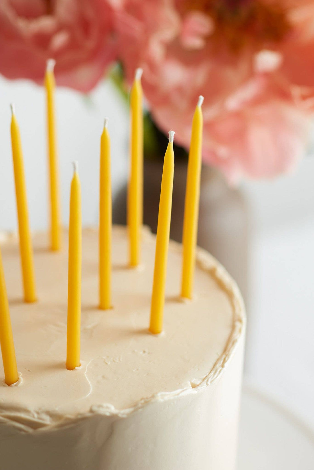 Traditional Beeswax Birthday Candles, slender yellow pure beeswax, with wicks, placed in a light-colored frosted cake,…