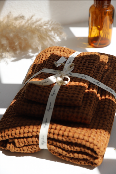 
                    
                      Terracotta Waffle Linen bath towel set, stacked and tied with a decorative white ribbon, close-up showing waffle texture.
                    
                  