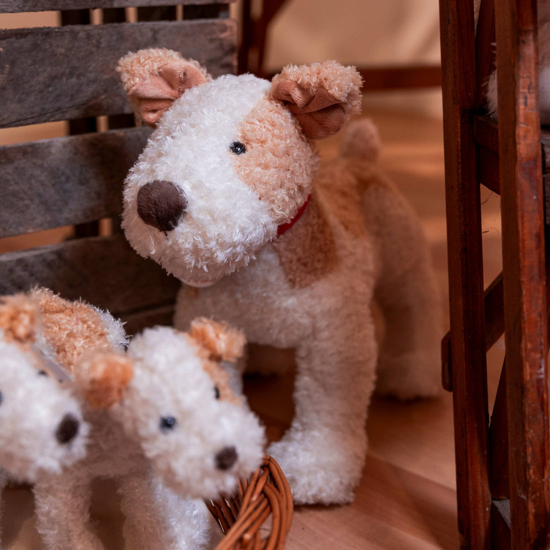 Eliot stuffed animal, white and light brown plush with red collar, standing behind two others in a wicker basket.