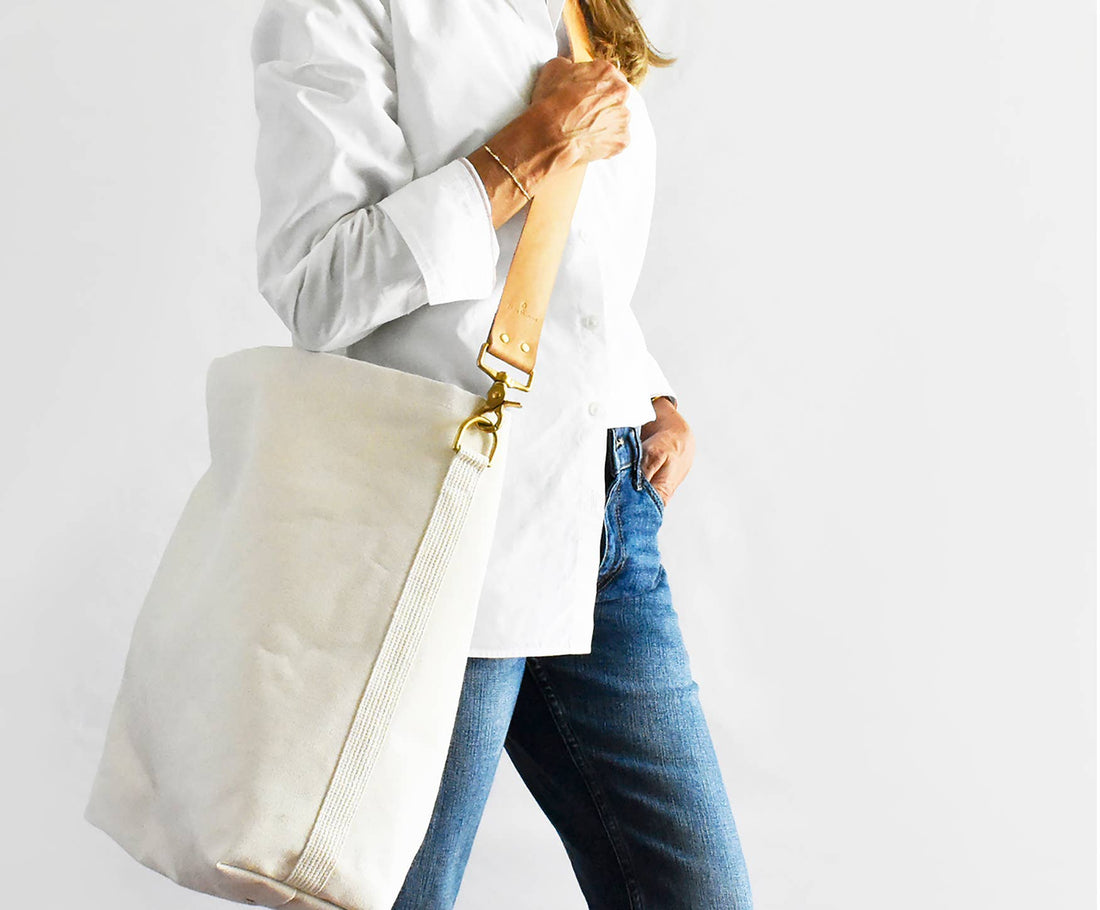 Everyday Tote bag, natural cotton canvas, worn over shoulder, showing tan leather strap and brass hardware detail.