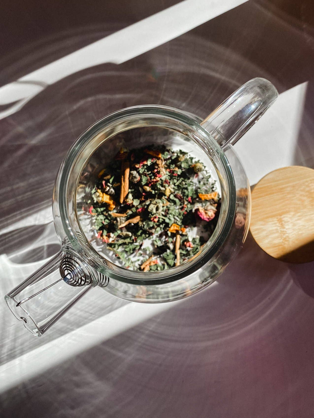 Borosilicate glass teapot, overhead view, with colorful loose leaf tea inside, visible stainless steel spiral infuser and…