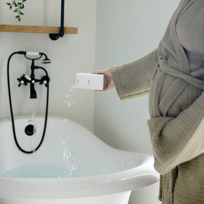 
                    
                      Magnesium Bath Soak, white magnesium chloride flakes pouring from its white tin into a running bath, showing product…
                    
                  