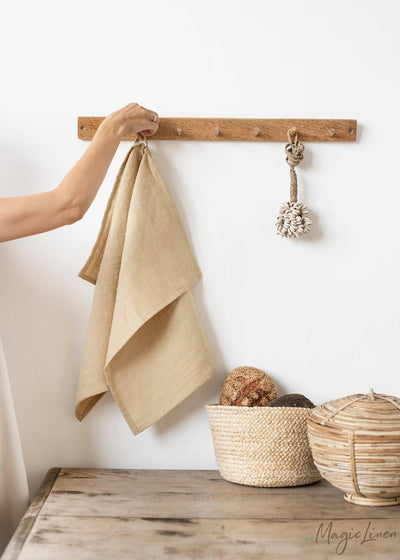 
                    
                      Premium Linen Tea Towel, natural beige, hand hanging it on a wooden peg rack, showcasing its soft linen texture.
                    
                  