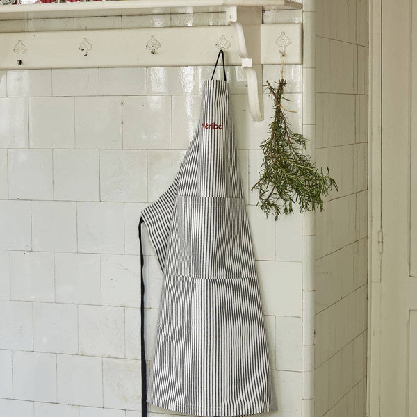 Sylvie Thiriez French Striped Cotton Apron, black and white vertical stripes, red 'Merbe' embroidery, hanging front view.