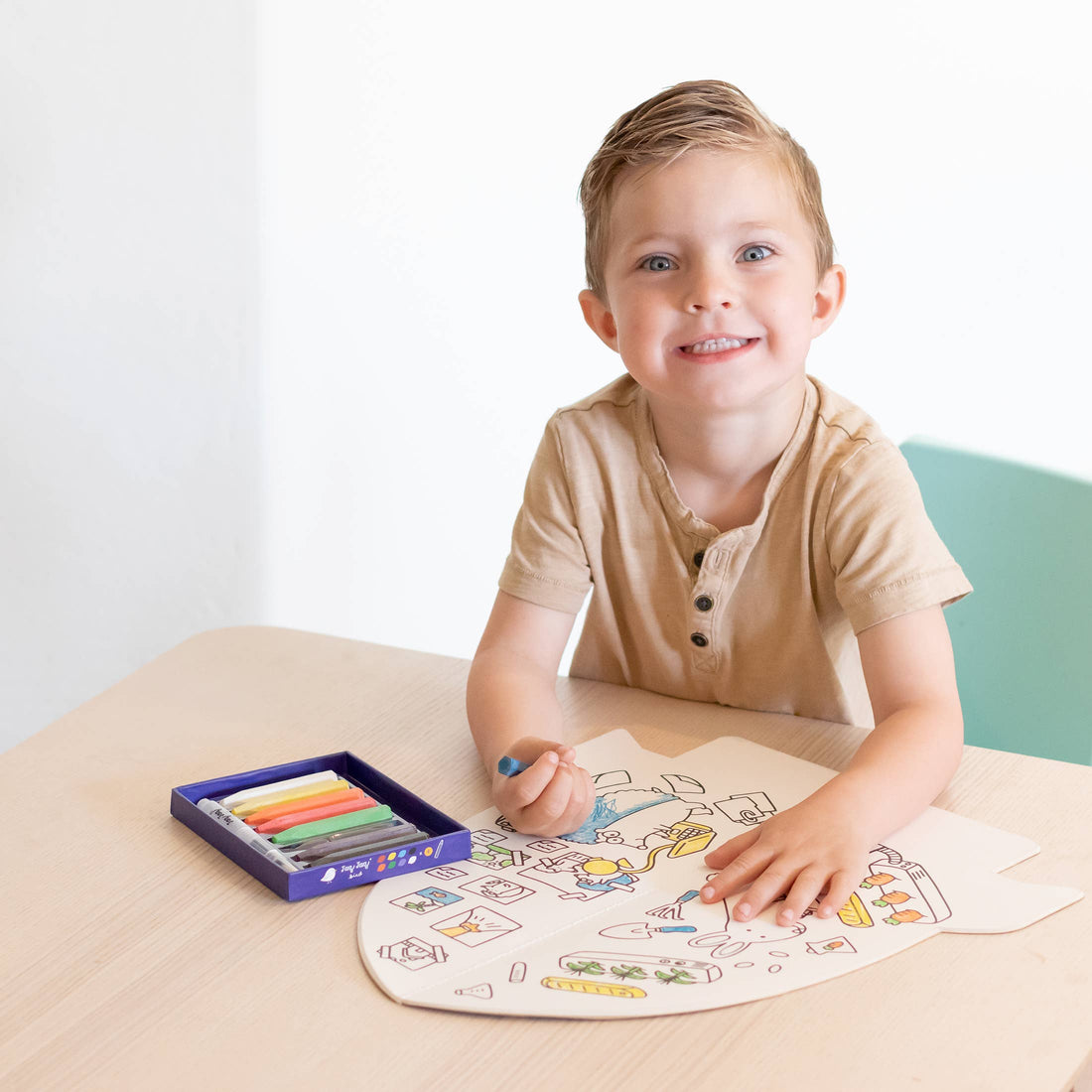 Jumbo Rocket Paper Coloring Book in-use, open on a light wood table. Child colors space-themed designs with a blue chalk…