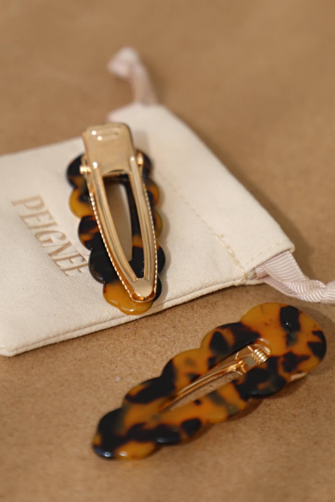 Signature hair clips (set of 2), tortoise acetate with gold-tone clasps. One clip on cream pouch, other showing clasp detail.