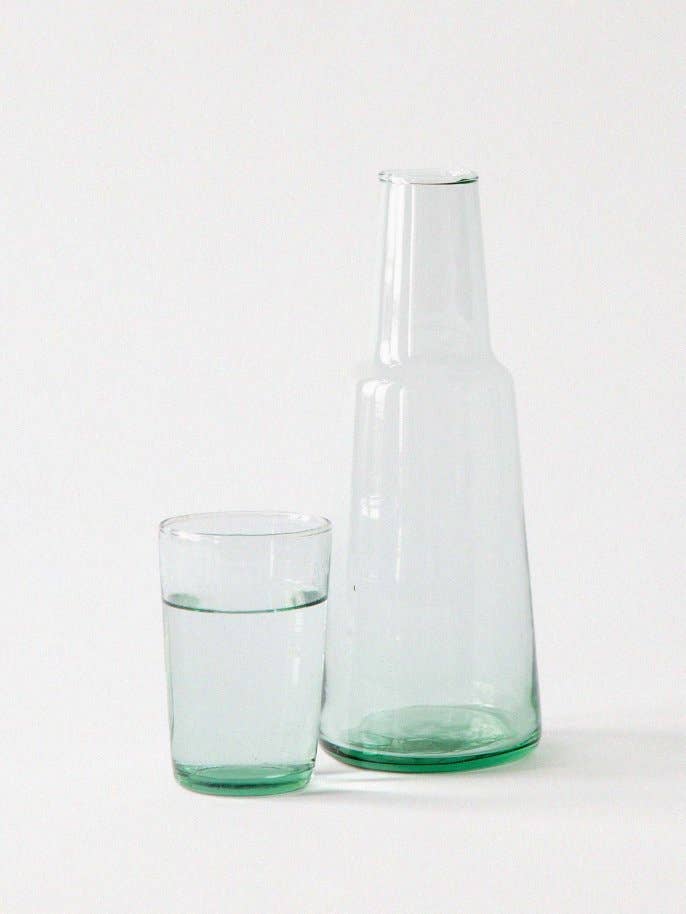 Lagonna Carafe, mouth-blown recycled glass with light green tint, shown next to a matching glass of water for scale.