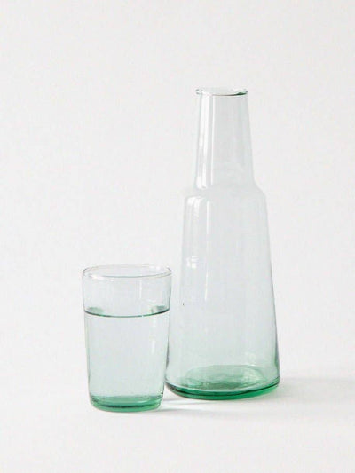 
                    
                      Lagonna Carafe, mouth-blown recycled glass with light green tint, shown next to a matching glass of water for scale.
                    
                  