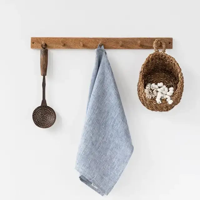 Light blue linen tea towel hanging from a wooden peg rail, showcasing its textured material and natural drape.