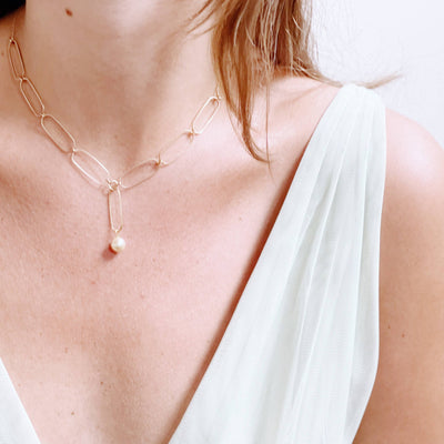 
                    
                      Paperclip And Pearl necklace, gold-toned paperclip chain with single cream pearl, worn on chest highlighting the Y-drop…
                    
                  