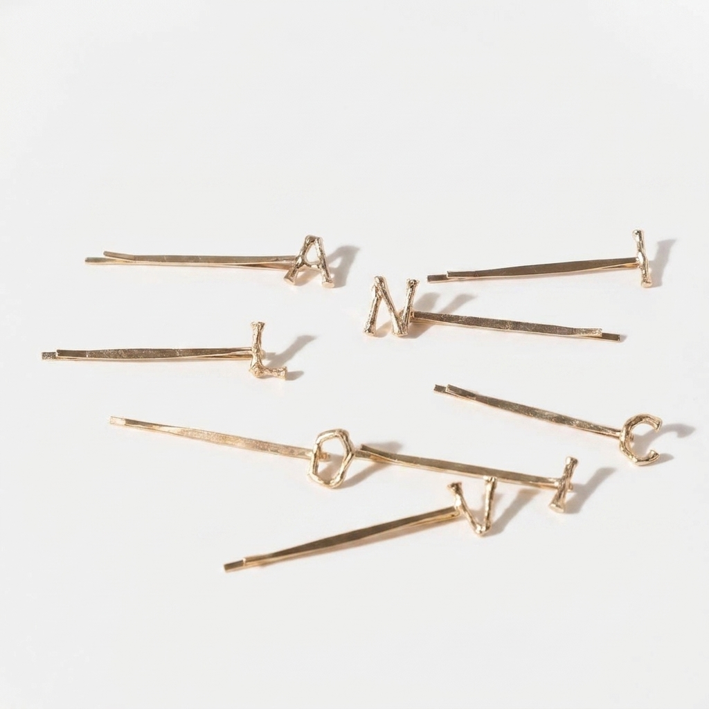 Peignee Paris Alphabet Letter gold-plated steel hair clips, featuring textured letters, scattered flat lay on white.